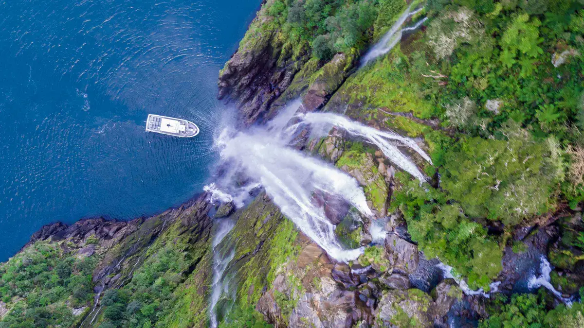 Small boat beneath a waterfall on a boutique Milford Sound boat tour in Fiordland, New Zealand