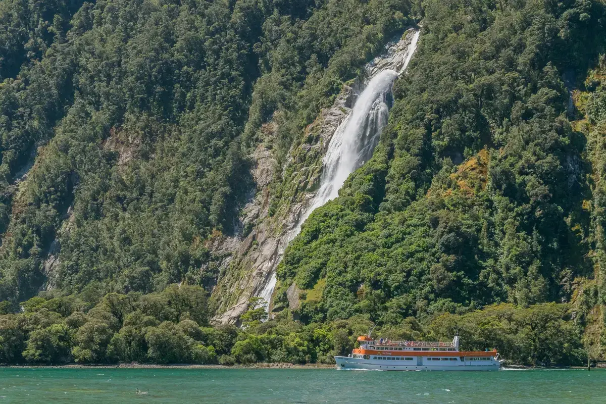 Bowen Falls dropping into Milford Sound with a cruise boat at its foot.