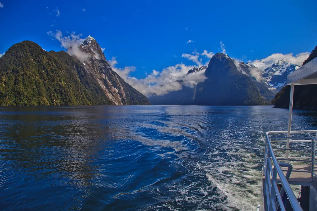 Blue water and snow-streaked peaks seen from the stern of a Milford Sound cruise boat.