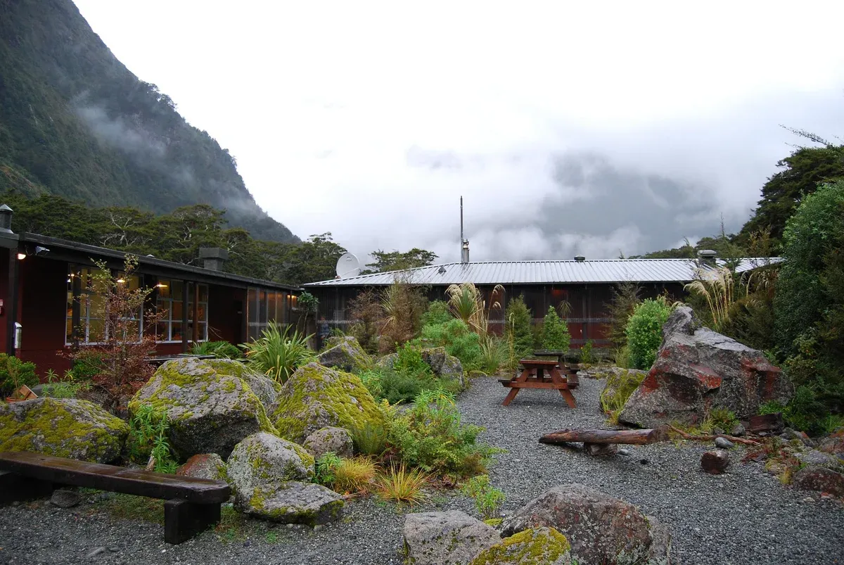 Milford Sound Lodge garden and buildings below cloud-covered peaks near Milford Sound.