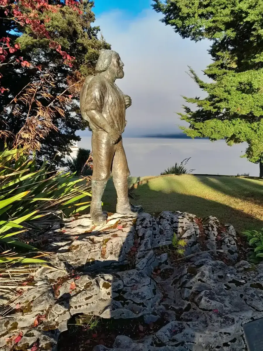 Statue of Quintin MacKinnon on the Te Anau lakefront with Lake Te Anau behind, a base for a Milford Sound cruise.