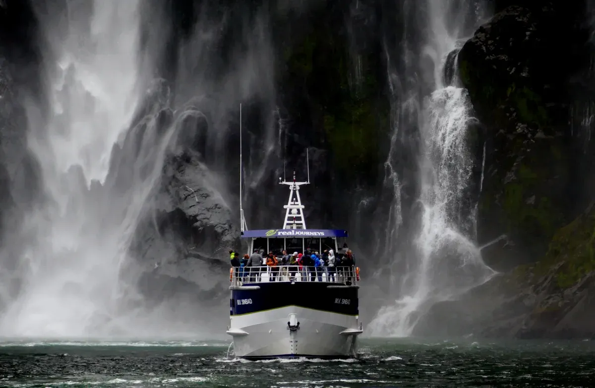 Passengers on the upper deck of a Milford Sound cruise boat facing a waterfall.