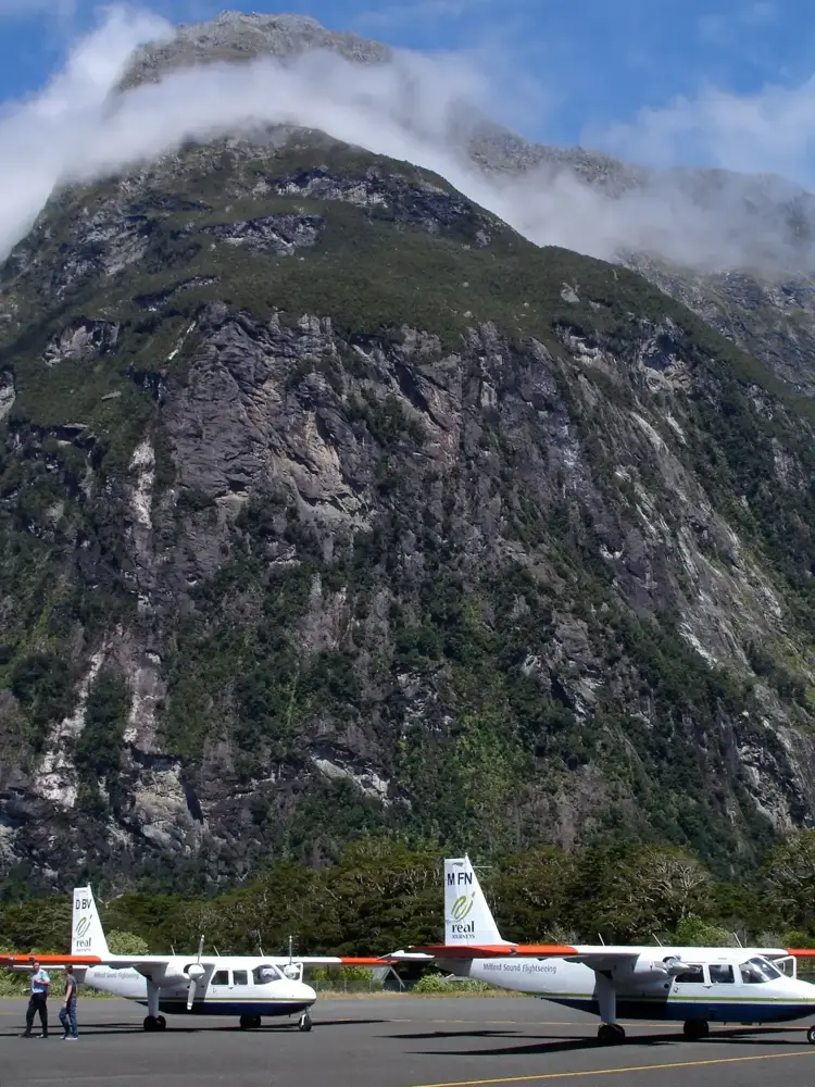 Light aircraft on the apron at Milford Sound Airport below a cloud-capped peak, for a Milford Sound cruise by air
