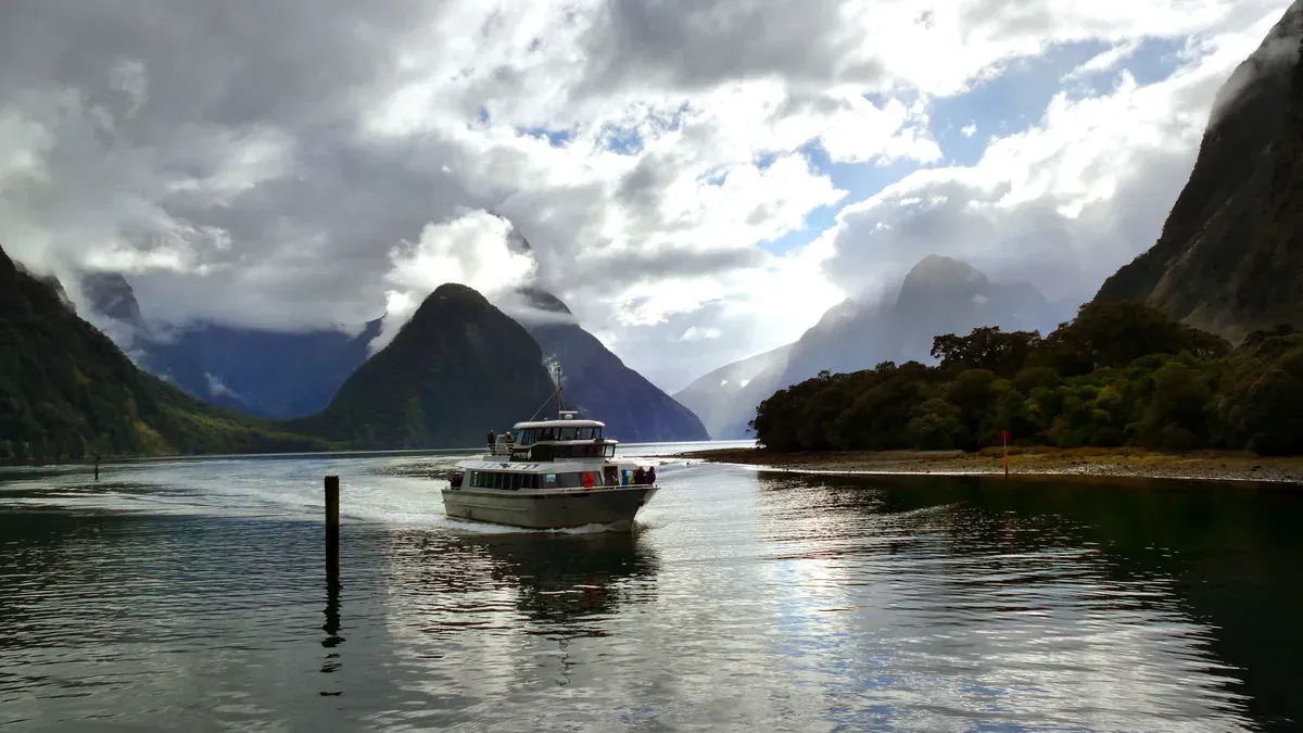 A small cruise boat on Milford Sound beneath cloud-capped peaks on a Milford Sound boat tour