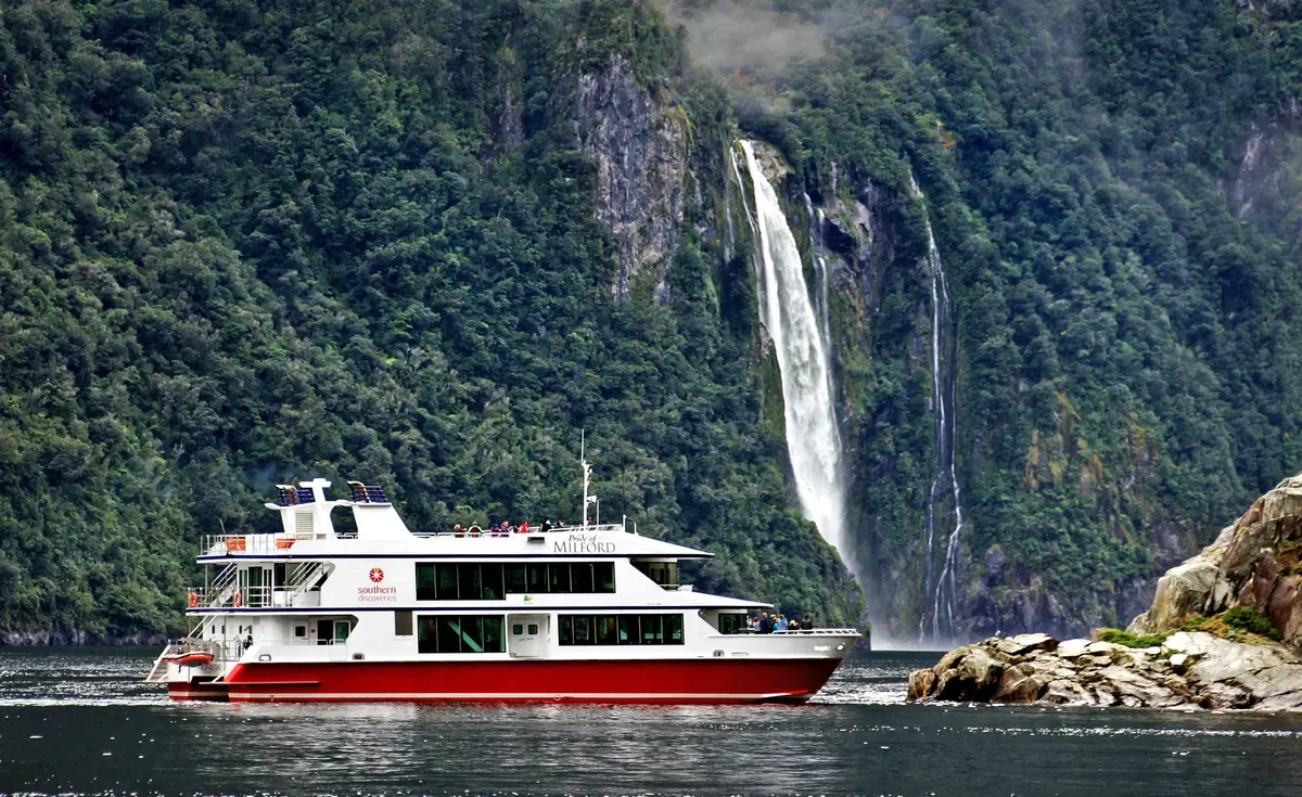 Pride of Milford catamaran below a tall waterfall on a Milford Sound cruise
